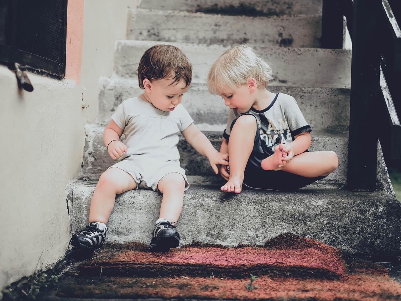 Dos niños de corta edad sentados sobre el primer escalón de una escalera de piedra buscando curiosamente algo que se les hubiera caído al suelo.