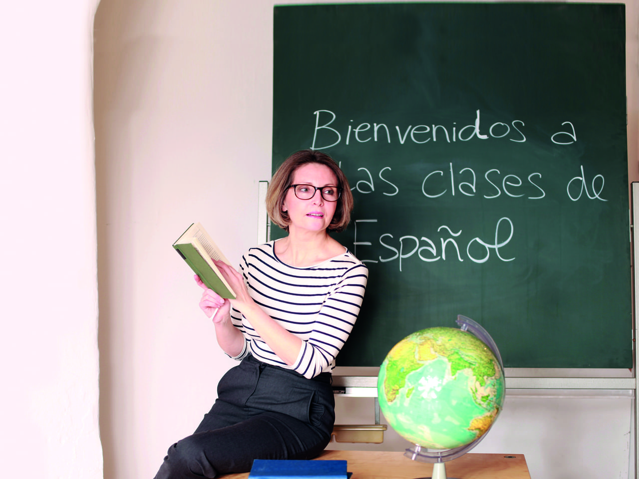 Profesora dando clases de español sentada sobre el borde de la mesa de un aula.