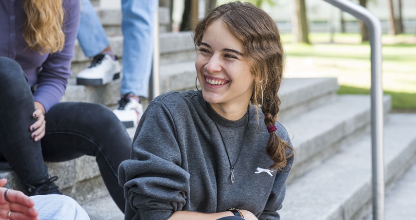 Imagen decorativa de una chica sonriendo sentada en las escaleras de la entrada del Centro de Estudios de Posgrado